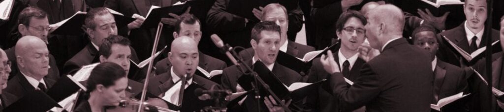 Conductor leading the Orpheus Male Chorus of Phoenix with violin accompaniment during a live performance.