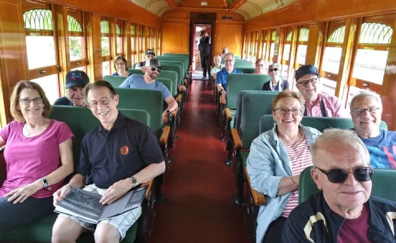 Members of the Orpheus Male Chorus of Phoenix smiling together on a group outing inside a vintage train car.