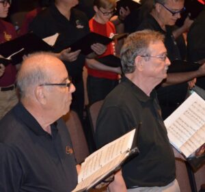 Ed Vivio, on the left, singing with a choir while holding sheet music.