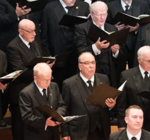 Ed Vivio, center bottom, singing with the choir in formal attire.