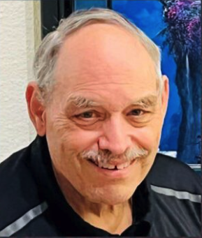 Bob Meier smiling in a portrait with a mustache, wearing a dark shirt.