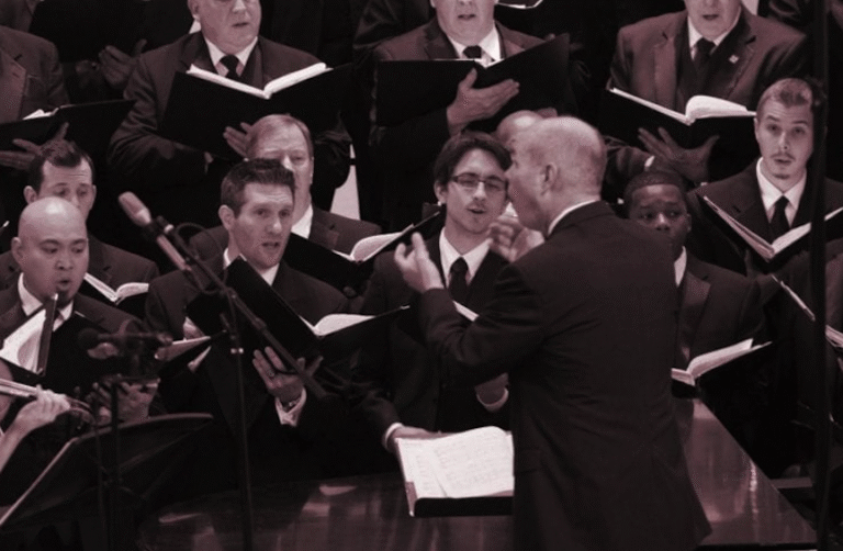 Conductor leading the Orpheus Male Chorus of Phoenix with violin accompaniment during a live performance.