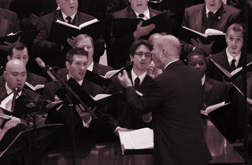 Conductor leading the Orpheus Male Chorus of Phoenix with violin accompaniment during a live performance.