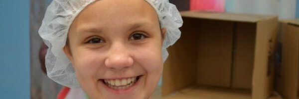Smiling child volunteer wearing a hairnet at a Feed My Starving Children charity event.