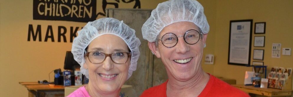 Two smiling volunteers wearing hairnets at a Feed My Starving Children charity event.