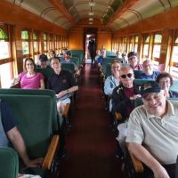 Bob Meier smiling on a train ride with Orpheus family, seated in the front row.