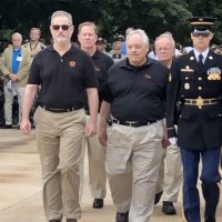 Bob Meier walking with fellow choir members during a ceremonial event alongside military personnel.
